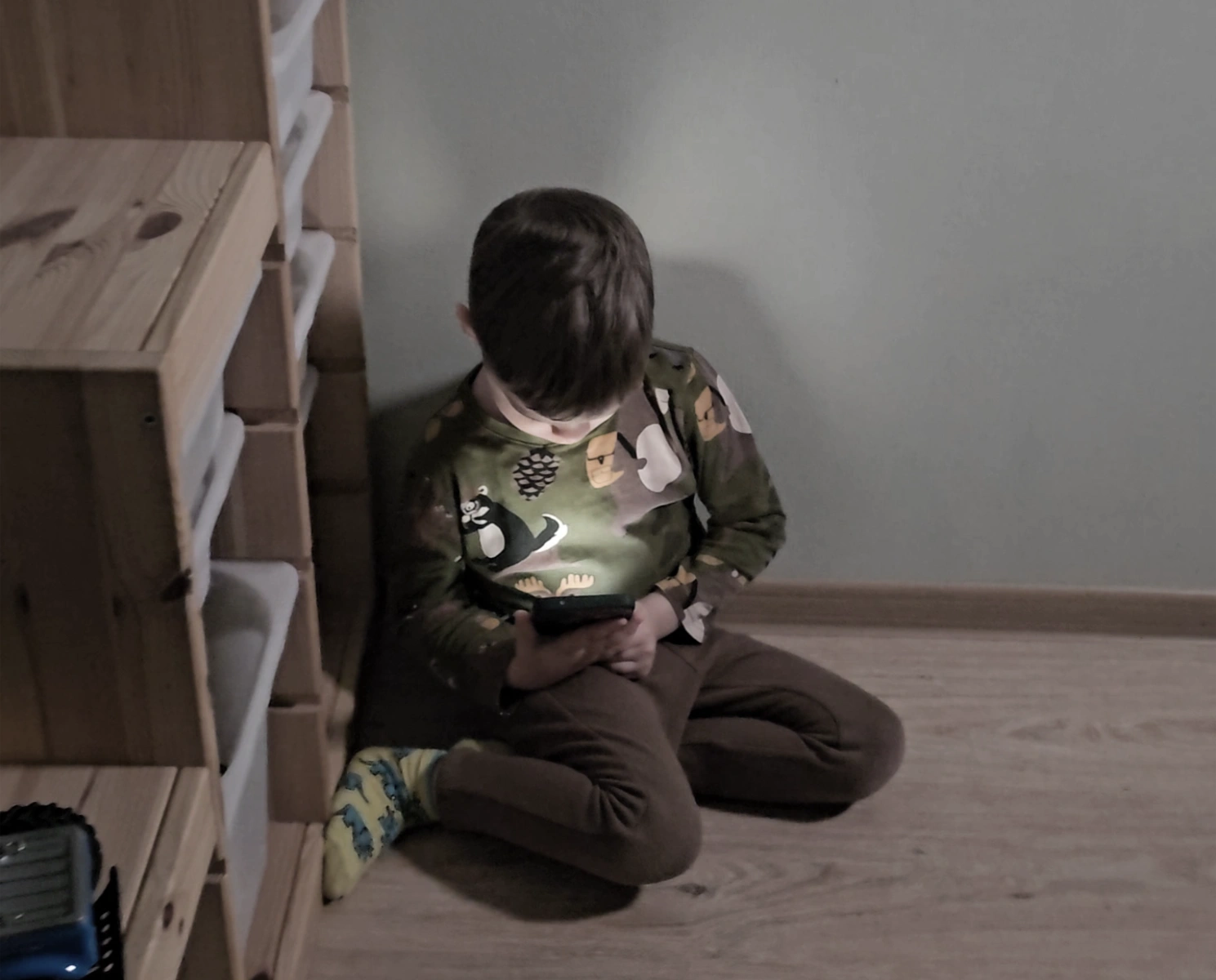 Child sitting in a dark corner looking down at a smartphone, showing passive screen time before discovering with a kids digital microscope